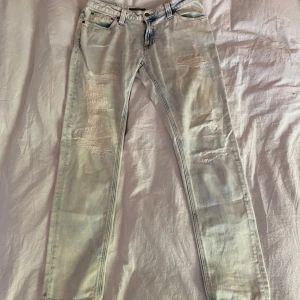 Nudie Jeans - Säljer ett par ljusblå jeans från Nudie Jeans med slitna detaljer och raka ben. Storlek W31 L30