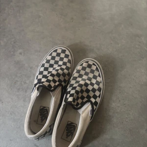 Vans slip-on checkerboard - Klassiska Vans slip-on med svartvitt rutigt mönster. Skorna har låg profil, vit sula och elastiska paneler på sidorna för enkel påtagning. Perfekta för en avslappnad och stilren look.