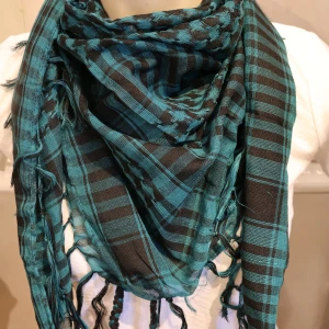 Turkos och svart rutig halsduk med fransar - Säljer en stor och mjuk turkos och svart halsduk med rutigt mönster och dekorativa fransar i kanterna. Perfekt att vira flera varv runt halsen för en cool look.