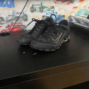 Svarta Nike sneakers med gulddetaljer - Säljer ett par svarta Nike sneakers med snygga gulddetaljer och svart sula. Skorna har snörning och en sportig design som passar perfekt till streetwear. Nike-loggan syns tydligt på sidan i guld. Och den har bara 4 hål men den är inte så stora