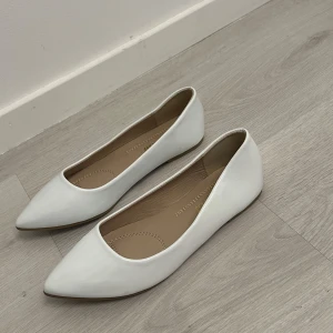 Vita ballerinaskor med spetsig tå - Säljer ett par stilrena vita ballerinaskor med spetsig tå och platt sula. Perfekta för dig som gillar en clean och klassisk look. Storlek 37 men sitter som 38,39. Helt oanvända för dom va för stora för mig 