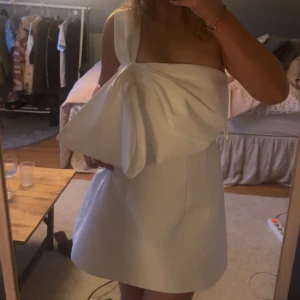 Kort vit klänning med stor rosett! - Jättesöt vit klänning med ett axelband och en stor rosett över bröstet! Perfekt till student eller avslutning!