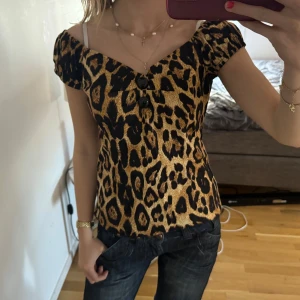 Leopardmönstrad topp från Collectif - Säljer en snygg topp från Collectif i leopardmönster. Toppen har korta ärmar, söt v-ringning och figurnära passform. 