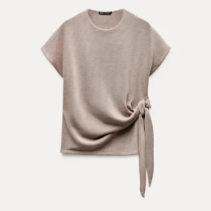 Beige topp med knyt i sidan - Snygg beige topp med rund halsringning och korta ärmar. Toppen har en unik knytdetalj i sidan som ger en cool och trendig look. Perfekt att styla med kjol eller jeans för en enkel men stilren outfit.