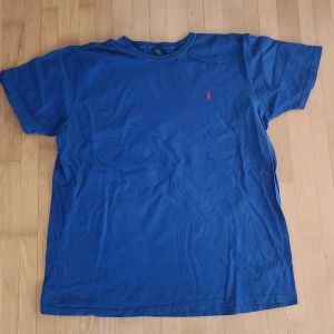 Blå t-shirt från Polo Ralph Lauren - Säljer en klassisk blå Ralph Lauren T-shirt med den ikoniska röda loggan broderad på bröstet – enkel, stilren och perfekt till sommaren! Den är i storlek XL men funkar utmärkt även för dig som har L, och ger en snygg oversized look på M. Tröjan är i mycket bra skick och passar både till vardags och mer avslappnade tillfällen. Originalpris ca 599 kr, mitt pris: endast 199 kr – ett riktigt fynd! 