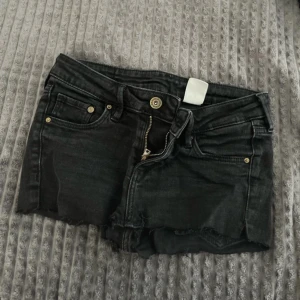 Svarta jeansshorts med rå kant - Svarta jeansshorts med klassisk femficksdesign och rå, avklippt kant nertill. Gylf med dragkedja och knapp framtill. Perfekta för varma dagar och enkel att matcha med olika toppar.