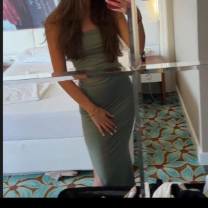 Olivgrön offshoulder långklänning - Snygg olivgrön långklänning med offshoulder-design och slits på sidan. Klänningen har en tight passform och är perfekt för sommarens tillfällen. Materialet är stretchigt och följsamt.