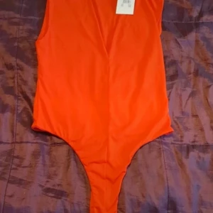 Klar-röd bodysuit från Bik Bok - Säljer en snygg röd bodysuit från Bik Bok. Modellen är ärmlös och har en enkel, stilren design. Tillverkad i stretchigt material med 93% polyester och 7% elastan. Perfekt att matcha med jeans eller kjol. Trådsläpp i urringningen som är lätt fixat för den händiga. Ny med prislapp.