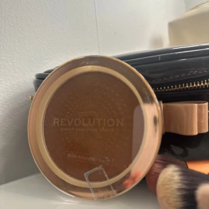 Revolution bronzer i guldbrun nyans - Pris kan diskuteras!Säljer en bronzer från Revolution i en varm guldbrun nyans. Kommer i en rund plastförpackning med transparent lock och guldfärgad kant. Perfekt för att ge ansiktet en solkysst look.