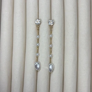 Långa örhängen med pärlor och kristall - Säljer ett par eleganta örhängen med gnistrande kristall upptill, tunn guldfärgad kedja och små vita pärlor samt en större pärla längst ner. Perfekta för att lyfta din stil.