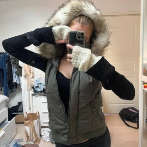 Grön västa - Snygg grön dunväst med stor luva kantad av fluffig fuskpäls. Västen har dragkedja framtill, två fickor med dragkedja och ribbad nederkant. Perfekt för lager-på-lager och ger en cool vibe till din outfit.