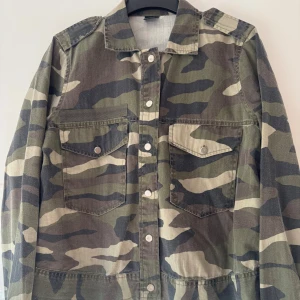 Camo jeansjacka från Gina Tricot - Snygg camouflagemönstrad jeansjacka från Gina Tricot i 100% bomull. Jackan har klassisk krage, knappar framtill och två bröstfickor med lock. Perfekt för dig som vill sticka ut med en streetig vibe. Använd två gånger.