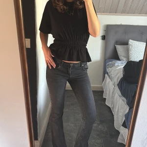 Svarta bootcut jeans - Säljer ett par svarta bootcut jeans med klassisk femficksdesign och låg midja. Jeansen har en snygg tvättad look och sitter tajt upptill med utsvängda ben. Perfekta för dig som gillar en tidlös och chill stil. 
