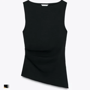 Svart asymmetrisk ärmlös topp - Svart ärmlös topp med asymmetrisk nederkant och figurnära passform. Snyggt draperad över magen för en cool och modern look. Perfekt att styla med både jeans och kjol för en trendig outfit.