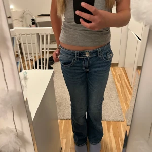 Blå bootcut jeans låg midja - Snygga blå jeans med bootcut och låg midja. Jeansen har klassiska fem fickor, ljus tvätt och lätt slitning på låren. Perfekta för en avslappnad och trendig look. Tillverkade i mjukt denimtyg som sitter skönt hela dagen. Skriv om ni har några frågor 