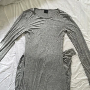 Grå långärmad klänning Gina Tricot - Säljer en enkel och stilren grå långärmad klänning från Gina Tricot i storlek XS. Klänningen har rund halsringning och är gjord i mjukt bomullsmaterial. Passformen är normal och längden är lång, liknar virala skims klänningen. Säljer pga den inte kommer till användning🫰🏻