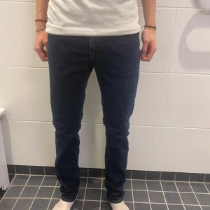 Mörkblå slim fit jeans Dressmann - Säljer ett par mörkblå slim fit jeans från Dressmann. Använda någon gång.  Klassisk trendig modell med snygga kontrastsömmar och normal midja. Jeansen är i bomull med lite stretch för skön passform och sitter tajt utan att bli för smala. Perfekt i dagens mode samt billiga för kvaliten. Nypris 600kr