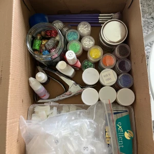 Nagelkit med borstar och glitter - Nagelkit med två nagellack (brun Gelook och rosa Maybelline Super Stay), nagellim från Technic och Ztiz, flera burkar med glitter i olika färger, penslar med lila skaft, blå fluffborste och metallverktyg för naglar. Perfekt för dig som älskar att fixa naglarna och vill ha många valmöjligheter.