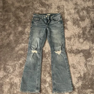 Ljusblå bootcut jeans med hål i knäna - Snygga ljusblå jeans ( Low waist/mid) från Gina tricot i storlek 164 och går att göra större och mindre i midjan, använda 1 gång bara så dom är som helt nya och fickor där bak💞