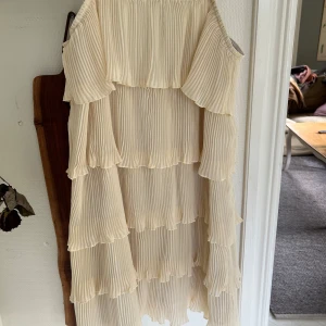 Champagnefärgad omlottklänning med volanger - Säljer en superfin champagnefärgad klänning med plisserade volanger i lager på lager. Klänningen har offshoulder och tunna axelband, vilket ger en luftig och romantisk vibe. Materialet är lätt och känns som polyester. Perfekt för sommarens alla tillfällen!
