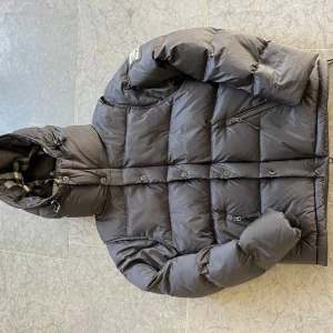 pufferjacka från Burberry - Kommer med tag sedan dustbag.  Passar även Small L. Säljer en svart pufferjacka från Burberry med stor huva och tydlig logga på ärmen. Jackan har dragkedjor, knappar och är tillverkad i polyester. Perfekt för kalla dagar och har en riktigt schysst oversized vibe.