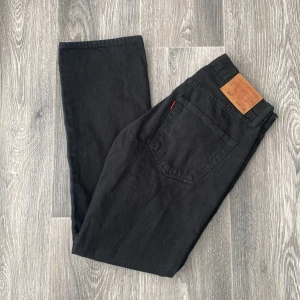 Svarta Levi's 501 jeans W31 L30 - Klassiska svarta Levi's 501 jeans med raka ben och femficksmodell. Jeansen har knappgylf, snygga nitar och den ikoniska läderpatchen bak i midjan. Tillverkade i robust bomullsdenim som ger en tidlös look.