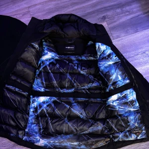 Svart vinterjacka från sail Racing Gore-Tex - Säljer en svart dunjacka från sail Racing med Gore-Tex-tyg. Jackan har huva, coola vita loggor på ärm och bröst samt en insida med blått och vitt mönster. Perfekt för kalla dagar och har dragkedja framtill. Jackan är lång och har en schysst passform. Jackan är xs men är väldigt stor i storleken så den sitter perfekt på s.