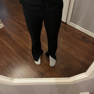 Svarta kostymbyxor från H&M - Snygga svarta kostymbyxor från H&M med rak passform och hög midja. Byxorna har klassisk look med vida ben och är tillverkade i ett mjukt tyg som känns bekvämt hela dagen. Perfekta för en clean och stilren outfit.