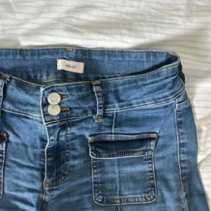 Blåa bootcut jeans med fickor från Nelly - orginalpris 560kr!! Snygga blåa bootcut jeans från Nelly med fina framfickor. Jeansen har dubbla knappar i midjan och markerade sömmar längs benen. Klassisk denimlook som passar till allt. Materialet är jeans och färgen är mellanblå.