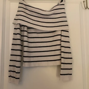 Randig offshoulder tröja från H&M - Säljer en ribbad offshoulder tröja från H&M i vitt med svarta ränder. Tröjan har lång ärm och en bred, nedvikt krage som ger en snygg offshoulder-look. Perfekt för dig som gillar en trendig och chill stil.