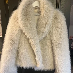 Fluffig vit pälsjacka med krage - Supermjuk och fluffig vit pälsjacka med bred krage och lång ärm. Jackan har en lyxig känsla och är perfekt för dig som vill sticka ut med en statement-piece.