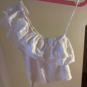 Vit volangtopp från Gina Tricot - Supersöt vit oneshoulder topp från Gina Tricot med volang och broderade spetsdetaljer. Hittar inte den på hemsidan så tror inte den säljs längre. Inga defekter och använd ca 10ggr🩷 Läs gärna bio🥰 OBS! Skriv innan köp säljer på fler ställen! Vill ni ha fler bilder så skriv💗💗