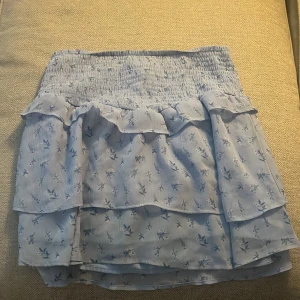 Blommig volangkjol från Gina Tricot - Supersöt ljusblå kortkjol från Gina Tricot med blommigt mönster och volangdetaljer. Kjolen har smock i midjan för en bekväm passform och är perfekt för vår och sommar. Tunn och luftig, passar till sneakers eller sandaler💓💓