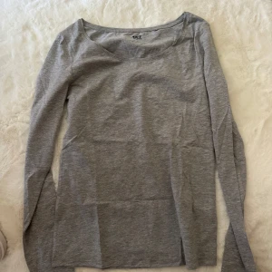 Grå långärmad tröja från 157 - En basic grå långärmad tröja från 157 i mjuk bomullsblandning. Tröjan har rundad halsringning och är figurnära utan att vara tight. Perfekt att styla med jeans eller kjol för en enkel och clean look.