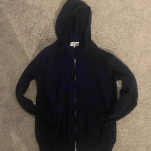 Mörkblå hoodie från Ahlquist Clothing  - Snygg mörkblå hoodie från Ahlquist Clothing i storlek S. Tröjan har huva, dragkedja framtill och långa ärmar. Materialet är stickat och känns mjukt mot huden. Perfekt för chill dagar eller när du vill ha en enkel och stilren look.