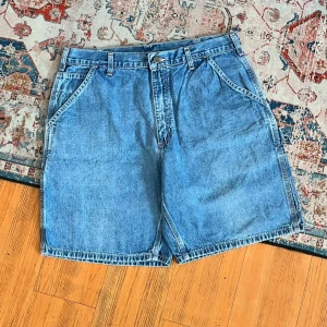Blå jeansshorts från Carhartt - Säljer ett par klassiska blå jeansshorts från Carhartt i 100% bomull. De har loose passform, flera stora fickor både fram och bak samt hällor för bälte. Perfekta för chill dagar och har en snygg, enkel look med robust känsla.