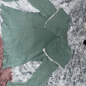 Grön stickad tröja med krage - Mysig grön stickad tröja med lång ärm och stor dekorativ krage med vit spetskant. Tröjan har en lätt loose passform och är tillverkad i en mjuk ullmix. Perfekt för dig som gillar vintagevibbar och unika detaljer.