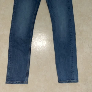 Blå jeansbyxor från 157, W30 L32 - Klassiska blå jeansbyxor från 157 med rak passform och normal midja. Jeansen har fem fickor, bälteshällor och snyggt tvättad denim. Perfekta för dig som gillar en enkel och tidlös stil. Materialet är slitstark bomullsdenim.