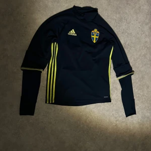 Svenska landslaget långärmad Adidas tröja - Mörkblå långärmad fotbollströja från Adidas med Sveriges landslagsemblem på bröstet och gula Adidas-logga. Snygga gula ränder längs sidorna och ärmarna. Tillverkad i funktionsmaterial (climacool) som andas. Perfekt för träning eller match.