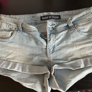 Ljusblå jeansshorts House of Denim - Supersnygga ljusblå jeansshorts från House of Denim med låg midja och tight passform. Shortsen har klassiska fickor, dragkedja och knappar framtill samt coola nitar och broderade detaljer på bakfickorna.lite små defekter där bak som har trillat av men annars e det i perfekt skick! Storlek s! 