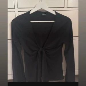 Svart långärmad knytblus - Snygg svart långärmad topp med v-ringning och knyt framtill. Aldrig använd