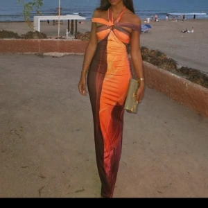 Färgstark långklänning med cut out - Säljer en maxad långklänning i orange, brun och lila med snygg cut out och ringdetalj framtill. Klänningen har offshoulder och halterneck, sitter tight och har ett coolt abstrakt mönster. Perfekt för dig som vill sticka ut och älskar färg!
