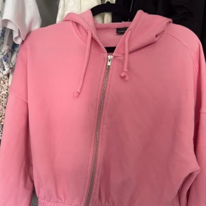 Rosa hoodiejacka från Gina Tricot - Säljer en rosa hoodiejacka från Gina Tricot i storlek S. Jackan har dragkedja framtill, huva med snörning och resår i midjan. Perfekt för en chill look och enkel att slänga på sig över allt. Mjuk bomullskänsla och långärmad modell.