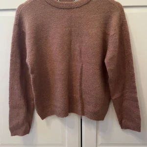 Stickad rosa tröja  - Mysig stickad tröja i en mjuk rosa ton med rund hals och långa ärmar. Tröjan har ribbade muddar vid hals, ärmslut och nederkant. Perfekt för dig som gillar enkel och chill stil. Som man kan se på bild tre så är lappen bortklippt.