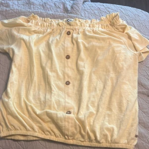 Gul offshoulder blus från Republic - Söt ljusgul offshoulder blus från Republic med korta ärmar och knappar framtill. Blusen har resår både upptill och nertill för en skön passform. Perfekt för varma dagar när du vill ha en luftig och trendig look.