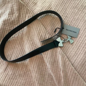 BALENCIAGA X UNDER ARMOUR BELT  (limited edition) - Säljer ett svart bälte i läder från Balenciagas collab med under armour förra året.  I äkta skinn med en unik, stor silverspänne i form av under armours logga. Skärpet har Balenciaga-logga både på lädret och spännet. Kommer med originalpåse och box. Perfekt statement piece för din outfit. Detta är nog ett av mina favvo saker jag äger men jag behöver pengarna för vintern så vill gärna bli av med den💔 Så va inte rädd att fråga frågor eller buda!!! :). Skicket är en 8,5/10, kvitto✅