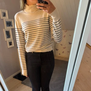 Randig polotröja i krämvit och svart - Snygg polotröja i krämvit med svarta  tunna ränder. Tröjan har lång ärm, hög krage och är i ett mjukt, tunt material som känns skönt mot huden. Använd 1 gång🩷