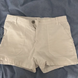 Vita shorts från KappAhl, storlek 36 - Snygga vita shorts från KappAhl i storlek 36. De har klassisk design med fickor både fram och bak, bälteshällor och stängs med knapp och dragkedja. Perfekta för varma dagar och lätta att matcha med allt. Materialet känns mjukt och skönt mot huden.