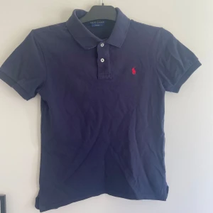 Marinblå pikétröja från Ralph Lauren - Tja, säljer denna skit snygga Ralph lauren piken som blivit för liten för mig, jag själv är 165 cm lång och passar någonstans under det. Det är stilren 14-16 år och är slimfit size, köpt ny för 1099kr, 9/10 skick! Hör av er om det är något. (Priset är ej hugget i stenen)