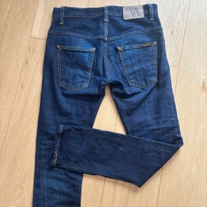 Selvedge jeans från Nudie Jeans Co - Säljer ett par Selvege jeans från Nudie Jeans Co i klassisk femficksmodell. Jeansen har kontrastsömmar i orange och raka ben med normal passform. Tvättade endast en gång och sparsamt använda. Modellen är utgången, men snarlik Grim tim. Hör av vid frågor!